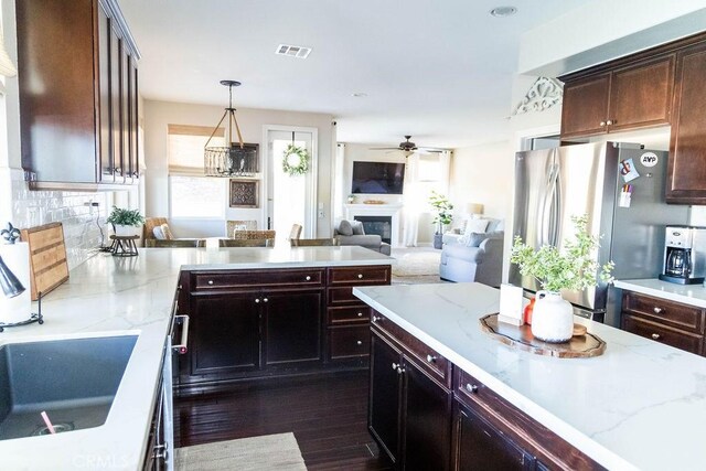 kitchen featuring dark wood-type flooring, tasteful backsplash, light stone counters, stainless steel fridge, and pendant lighting