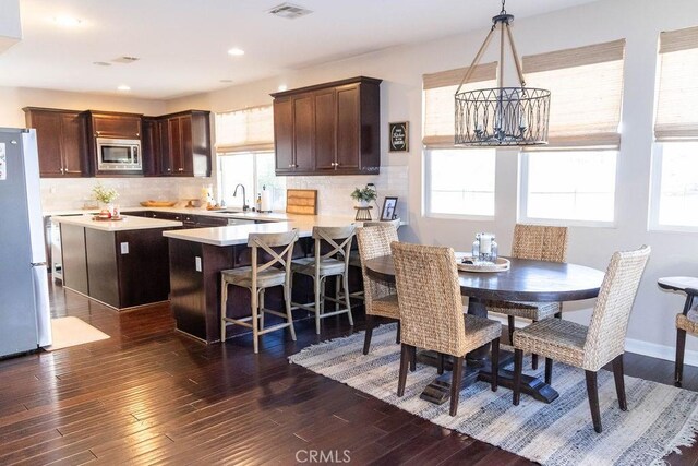 kitchen with a wealth of natural light, pendant lighting, stainless steel microwave, and refrigerator