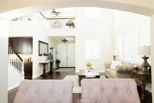 living area with stairway, baseboards, a towering ceiling, dark wood-style floors, and ceiling fan