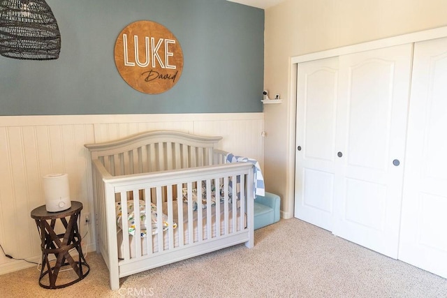 carpeted bedroom with wainscoting, a closet, and a crib
