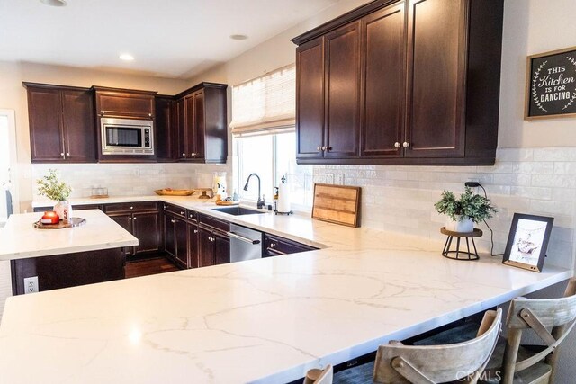 kitchen with sink, appliances with stainless steel finishes, a kitchen bar, decorative backsplash, and kitchen peninsula