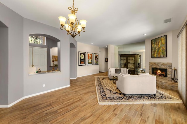 living room featuring an inviting chandelier, a stone fireplace, and light hardwood / wood-style floors