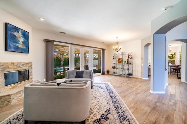 living room with french doors, a stone fireplace, a chandelier, and light hardwood / wood-style flooring