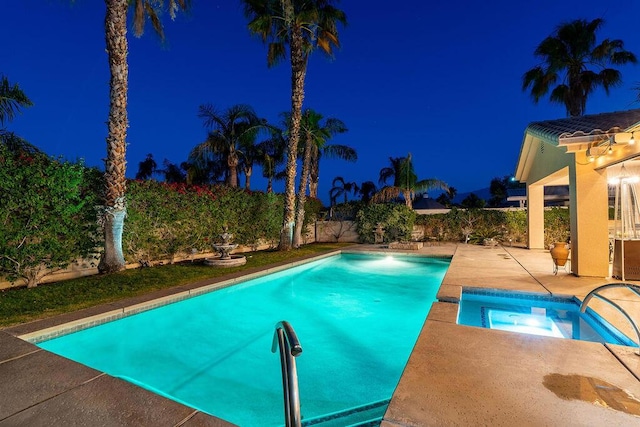 pool at night with a patio area and an in ground hot tub