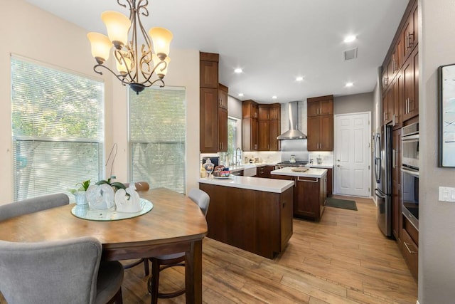 kitchen featuring wall chimney exhaust hood, decorative light fixtures, a chandelier, a center island, and appliances with stainless steel finishes