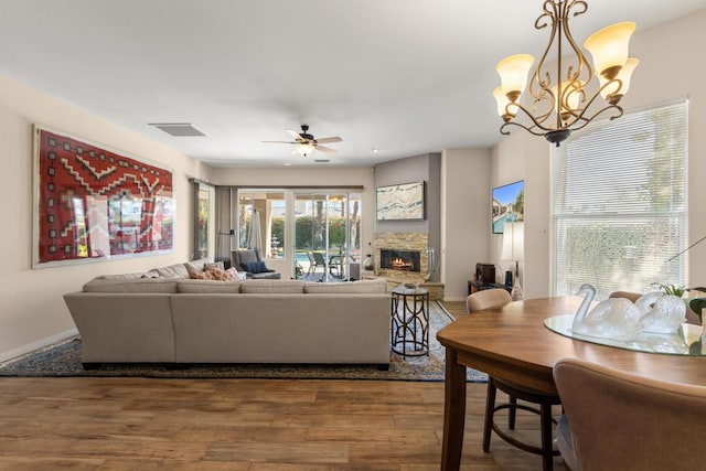 living room with ceiling fan with notable chandelier, a stone fireplace, and dark hardwood / wood-style floors