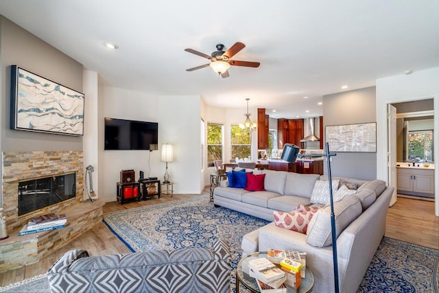 living room with a stone fireplace, ceiling fan with notable chandelier, and light hardwood / wood-style floors