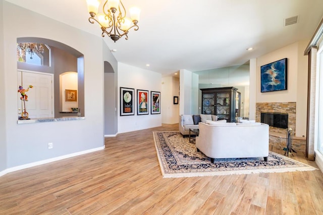 living room featuring a stone fireplace, a chandelier, and light wood-type flooring