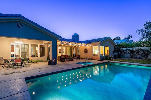 pool at dusk featuring an in ground hot tub and a patio