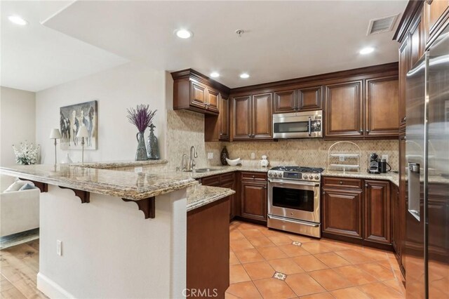 kitchen with a breakfast bar, sink, tasteful backsplash, kitchen peninsula, and stainless steel appliances