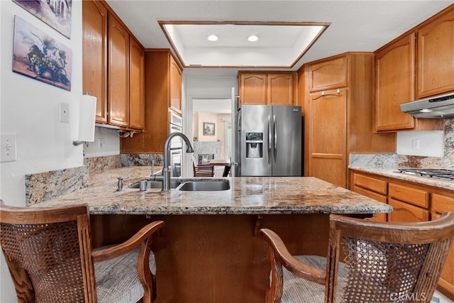 kitchen featuring a raised ceiling, sink, a breakfast bar area, kitchen peninsula, and stainless steel appliances