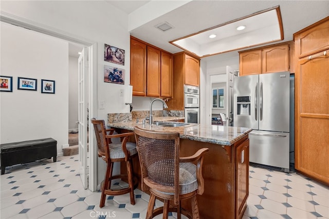 kitchen with sink, light stone counters, a tray ceiling, kitchen peninsula, and stainless steel appliances