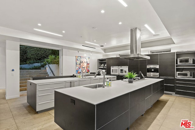 kitchen with white cabinetry, sink, a large island with sink, island exhaust hood, and light tile patterned floors