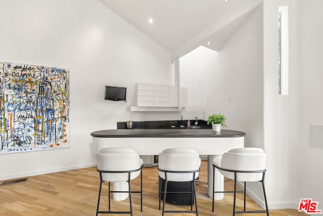 bar featuring high vaulted ceiling, light hardwood / wood-style floors, sink, and white cabinets