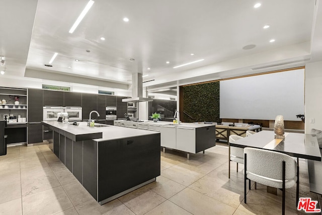 kitchen with island exhaust hood, a large island, sink, and backsplash