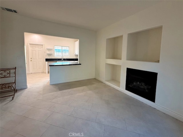 unfurnished living room featuring sink, light tile patterned floors, and built in features