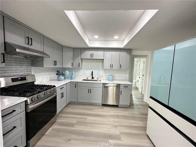 kitchen with stainless steel appliances, gray cabinets, a raised ceiling, and sink