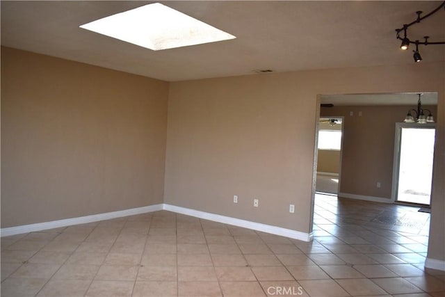 tiled empty room with a notable chandelier and a skylight