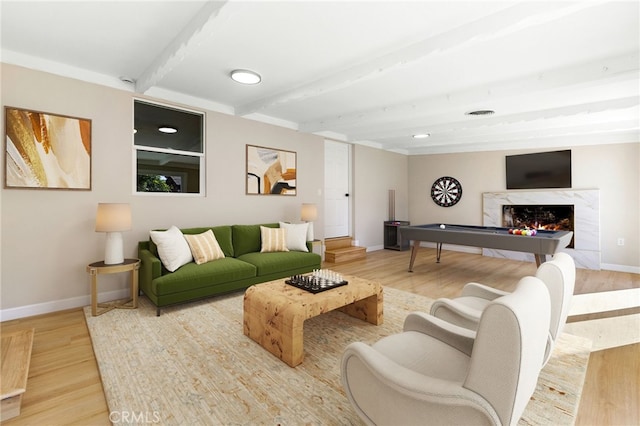 living room featuring wood-type flooring, a premium fireplace, and beamed ceiling