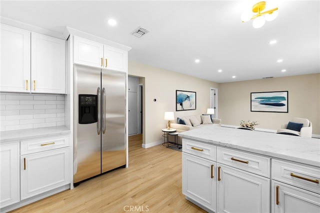 kitchen with white cabinetry, backsplash, stainless steel refrigerator with ice dispenser, light stone counters, and light hardwood / wood-style floors