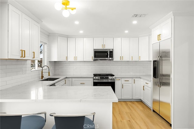 kitchen featuring appliances with stainless steel finishes, a breakfast bar, sink, white cabinets, and kitchen peninsula