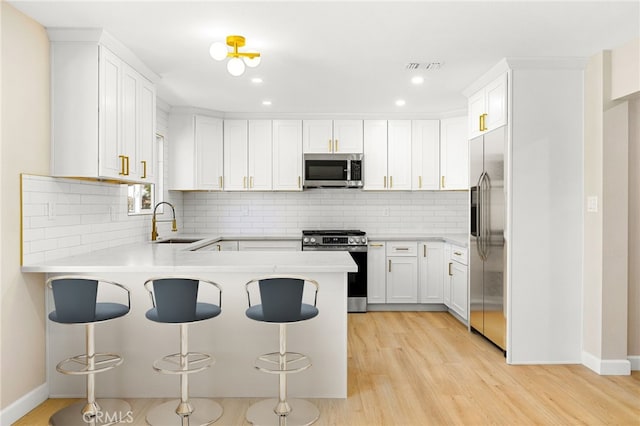 kitchen featuring sink, a breakfast bar area, appliances with stainless steel finishes, white cabinets, and kitchen peninsula