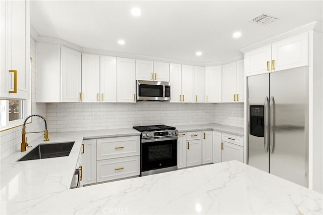 kitchen featuring sink, light stone counters, white cabinetry, appliances with stainless steel finishes, and backsplash