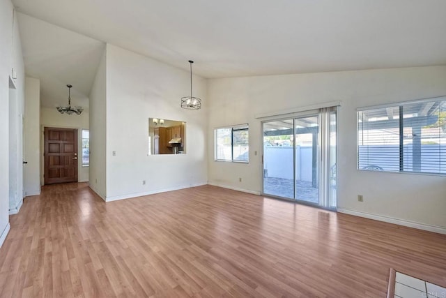 unfurnished living room with a notable chandelier, high vaulted ceiling, and light wood-type flooring