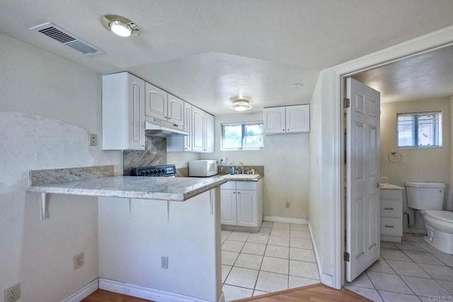 kitchen with light tile patterned floors, sink, kitchen peninsula, and white cabinets