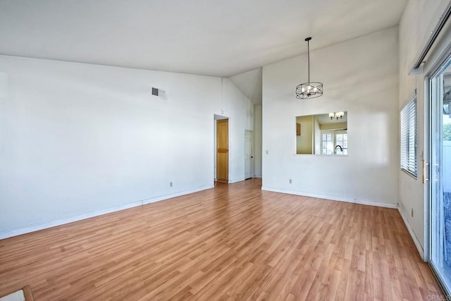 empty room featuring an inviting chandelier, high vaulted ceiling, and light hardwood / wood-style floors