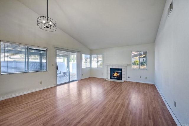 unfurnished living room with a tile fireplace, wood-type flooring, high vaulted ceiling, and a chandelier