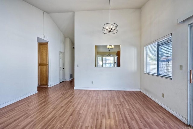 interior space with a high ceiling, ceiling fan with notable chandelier, and light wood-type flooring