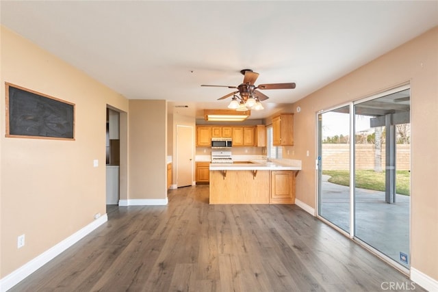 kitchen featuring a breakfast bar, range, dark hardwood / wood-style floors, kitchen peninsula, and light brown cabinets