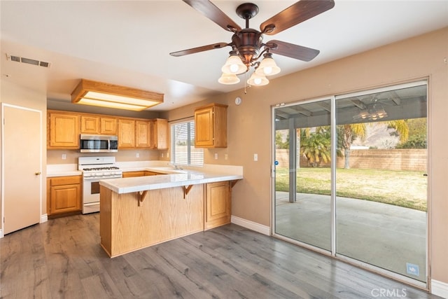 kitchen with dark wood-type flooring, a breakfast bar, gas range gas stove, light brown cabinets, and kitchen peninsula