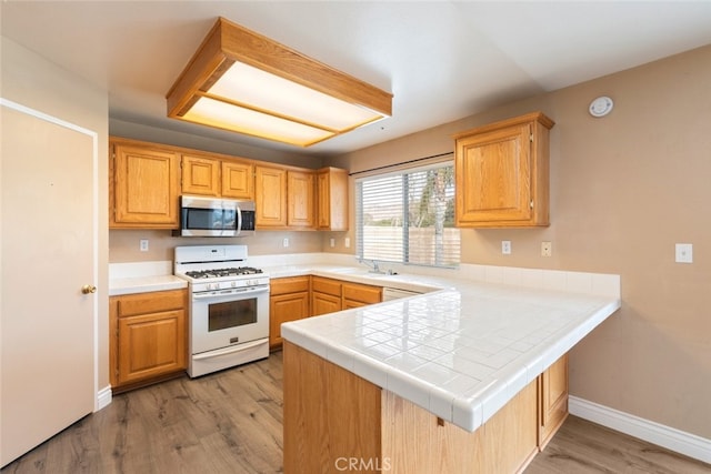 kitchen featuring white gas range, kitchen peninsula, sink, and light hardwood / wood-style flooring