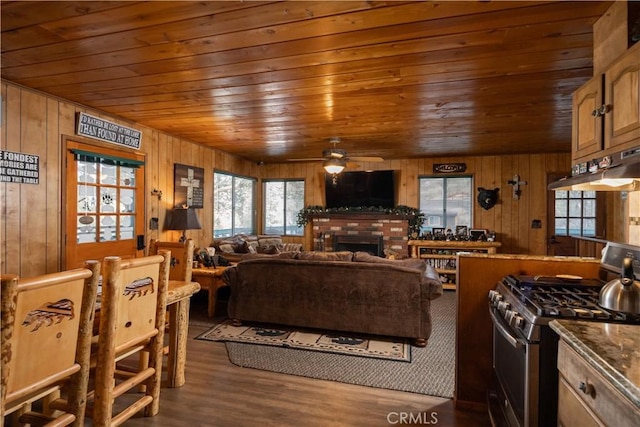 living room featuring dark wood-type flooring, ceiling fan, wooden walls, a fireplace, and wooden ceiling