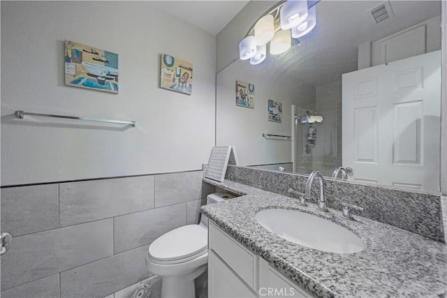 bathroom featuring tile walls, vanity, toilet, and walk in shower