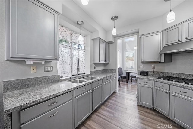 kitchen featuring dark wood-type flooring, stainless steel gas cooktop, sink, gray cabinets, and pendant lighting