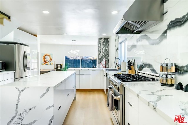 kitchen with decorative light fixtures, appliances with stainless steel finishes, white cabinets, light stone countertops, and exhaust hood