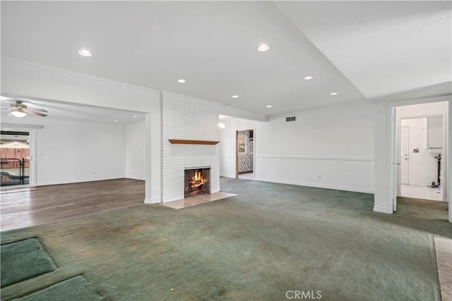 unfurnished living room featuring ceiling fan, dark carpet, and a fireplace