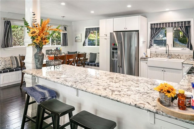 kitchen featuring light stone counters, high end refrigerator, sink, and a breakfast bar area