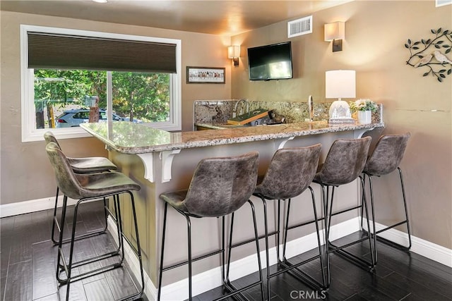 bar featuring dark wood-type flooring and light stone countertops