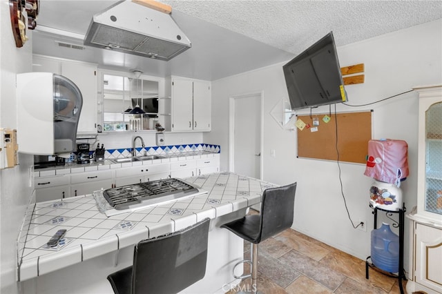 kitchen with sink, a breakfast bar, white cabinetry, tile countertops, and stainless steel gas stovetop