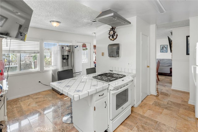 kitchen featuring a breakfast bar area, stainless steel fridge, white gas range oven, white cabinets, and tile countertops