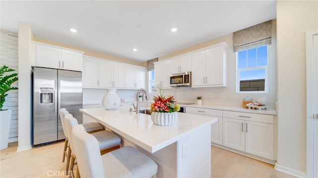 kitchen featuring stainless steel appliances, an island with sink, a wealth of natural light, and white cabinets