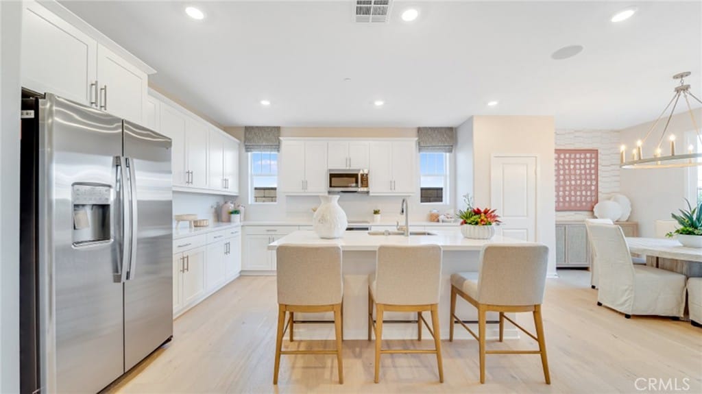 kitchen with light hardwood / wood-style flooring, hanging light fixtures, a center island with sink, appliances with stainless steel finishes, and white cabinets