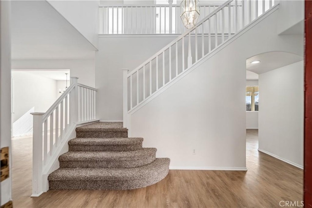 staircase featuring a towering ceiling, hardwood / wood-style floors, and a chandelier