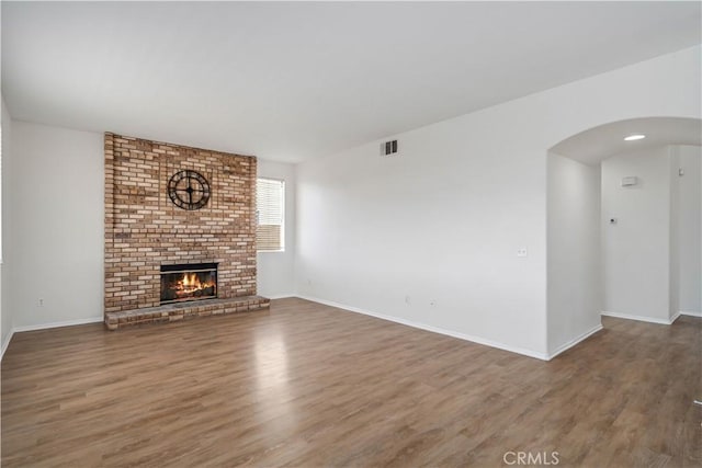 unfurnished living room with dark wood-type flooring and a brick fireplace