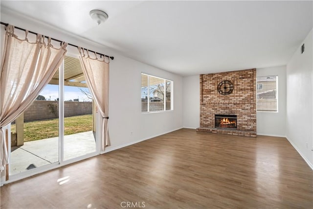 unfurnished living room with dark wood-type flooring, a healthy amount of sunlight, and a brick fireplace