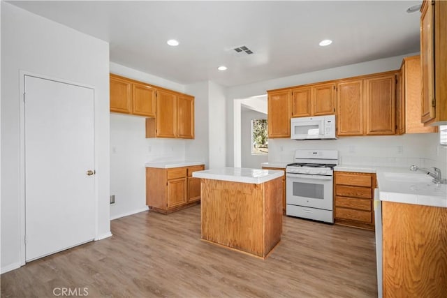 kitchen with white appliances, a center island, sink, and light hardwood / wood-style flooring